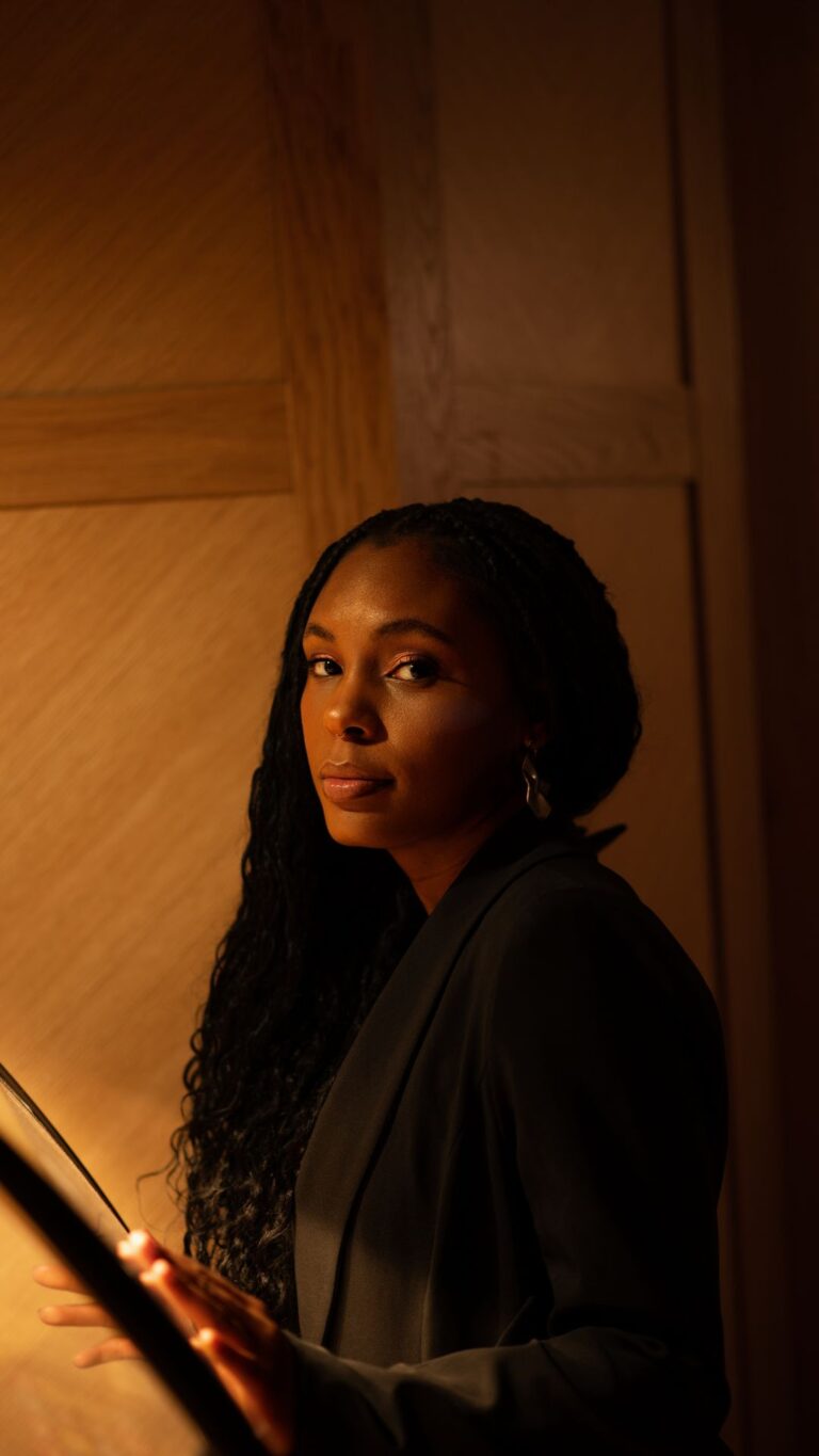 Black woman standing in front of a juke box with warm lighting on her face